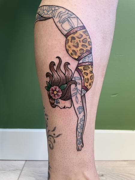 Traditionele tattoo van een lenige vrouw in panterprint pak op onderbeen.