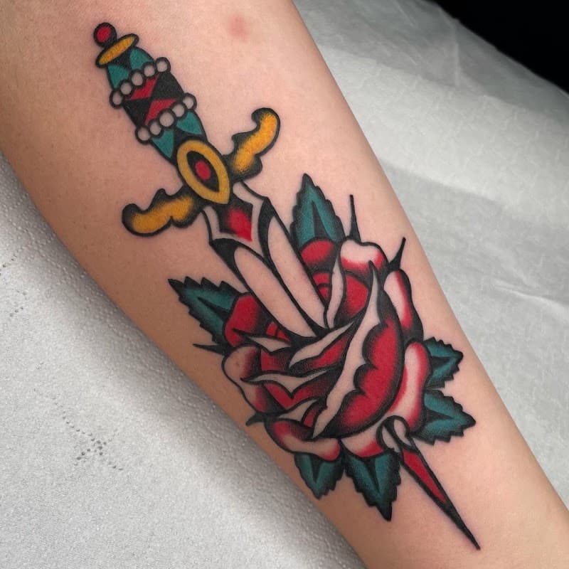 Traditional tattoo van een dolk door een roos op de onderarm.