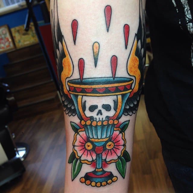Traditionele tattoo van een kelk met schedel, vleugels en bloemen.
