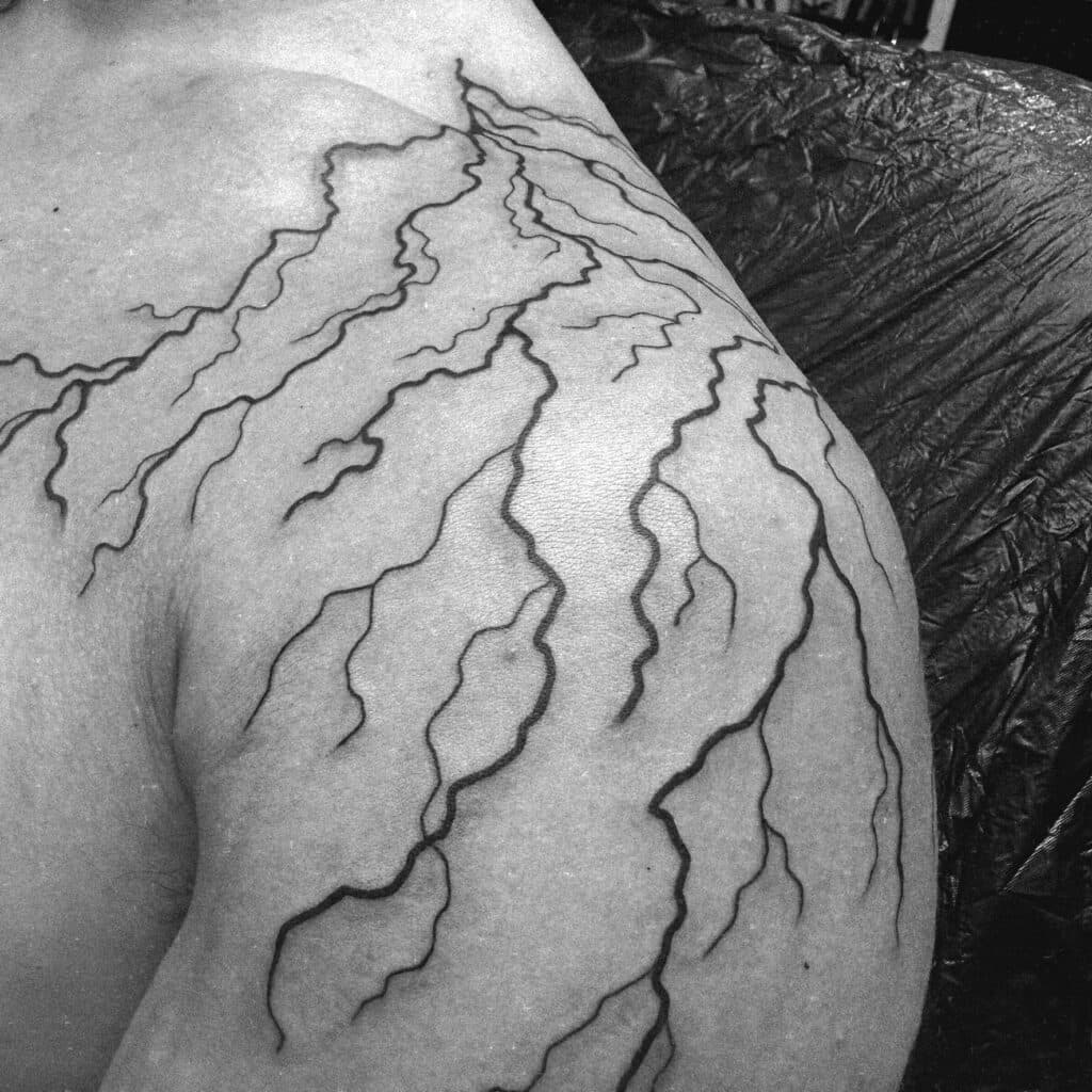 Grote blackwork bliksem tattoo op schouder en bovenarm.