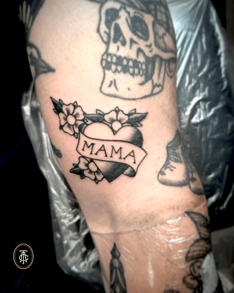 Traditioneel hart met 'MAMA' banner en bloemen op de bovenarm.