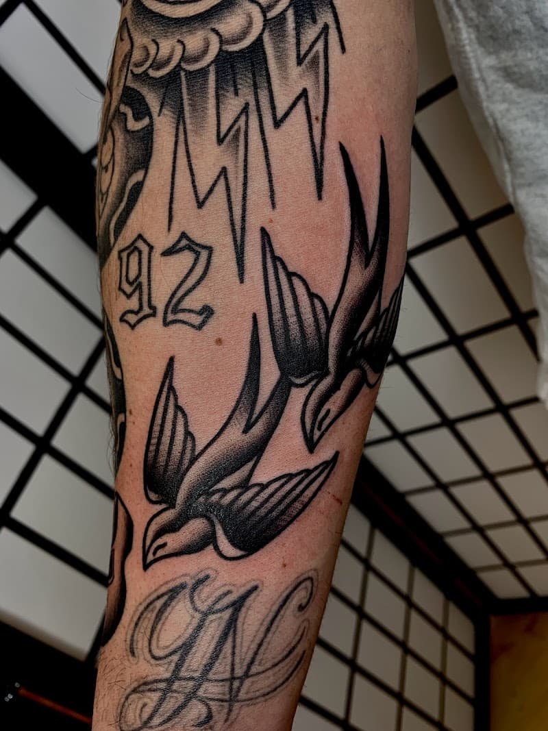 Twee traditionele zwaluwen in zwart-wit op een onderarm.