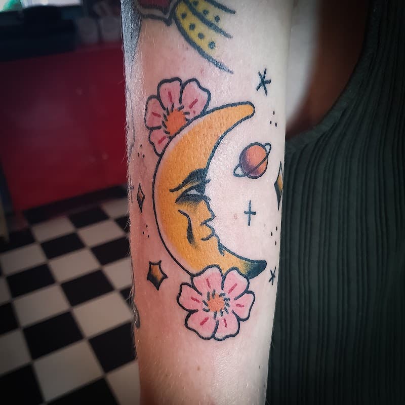 Traditional tattoo van een halve maan met gezicht, bloemen en een planeet.