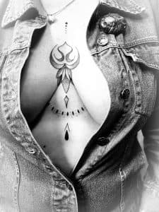 Zwart-wit ornamental tattoo op borstbeen met lotus en stippen.