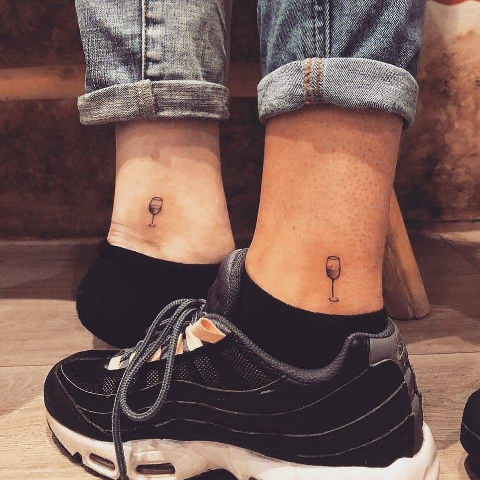 Twee kleine, minimalistische wijnglas tattoos op de enkels.