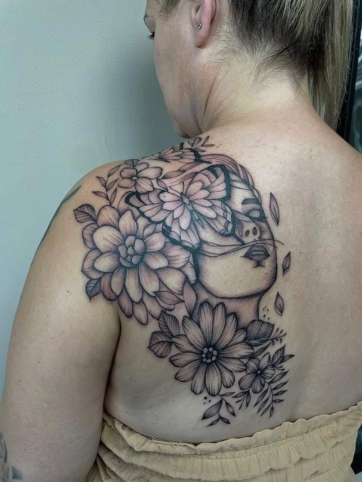 Vrouwengezicht met vlinder en bloemen op schouderblad.