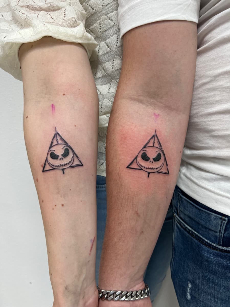 Twee identieke Jack Skellington Deathly Hallows tattoos op onderarmen.