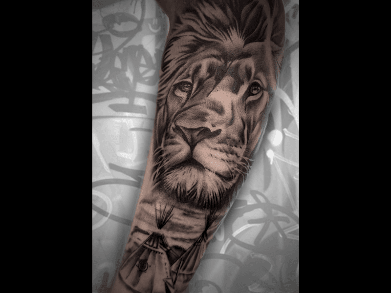 Realistische leeuwenkop met daaronder tipi's in een landschap op de onderarm.