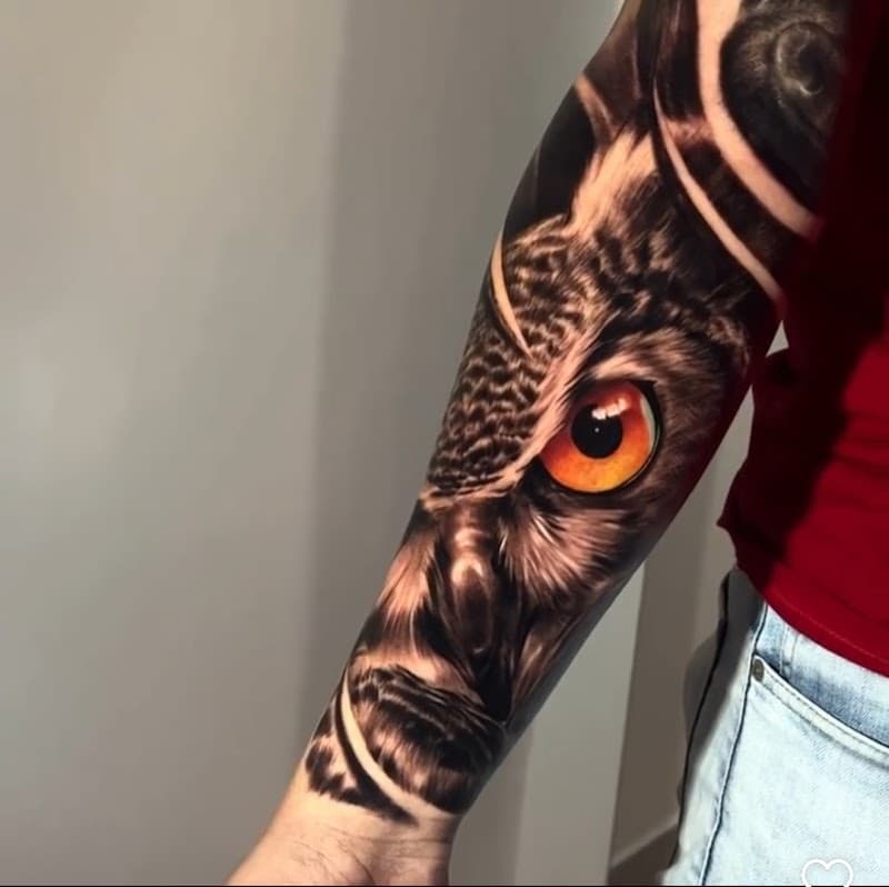 Realistische uil met fel oranje oog op onderarm.