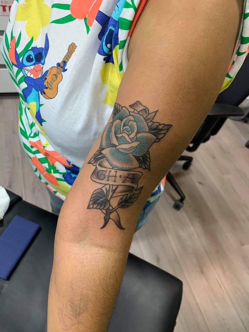 Blauwe roos met banner en letters 'GHA' op bovenarm.