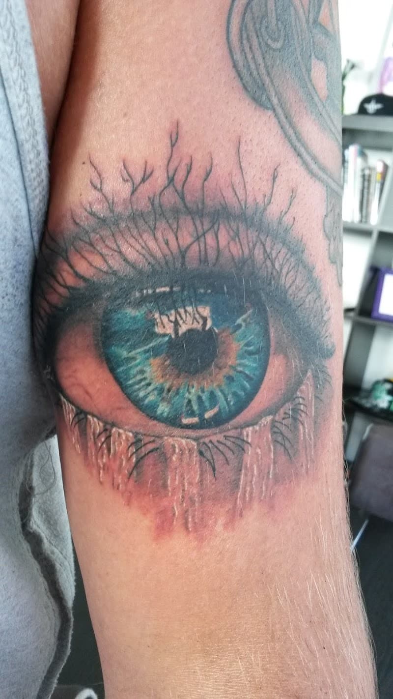 Realistisch oog met blauwe iris en boomwortels op bovenarm.