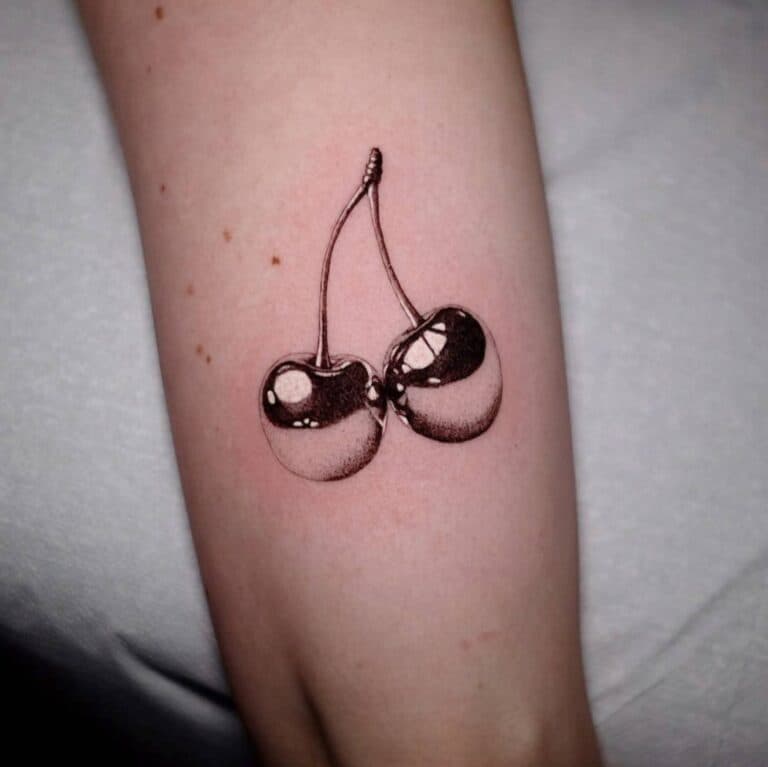 Realistische chromen kersen tattoo in zwart-wit op de arm.