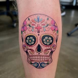 Kleurrijke sugar skull tattoo met bloemen en kruis op het onderbeen.