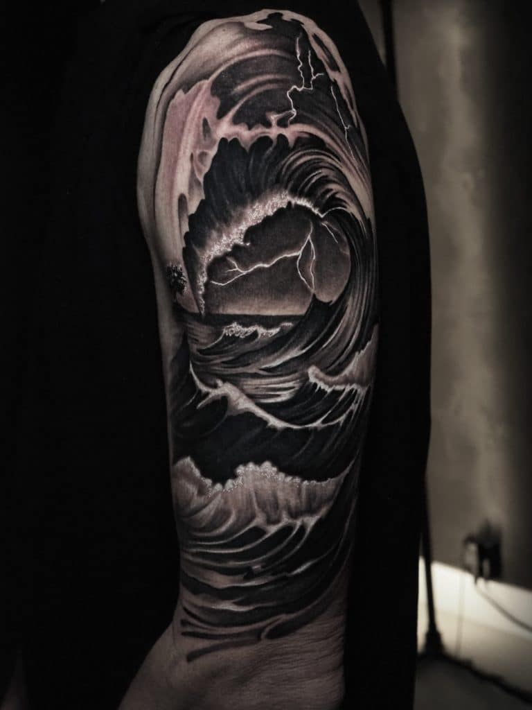 Zwart-wit tattoo van stormachtige zee met grote golf en bliksem op bovenarm.