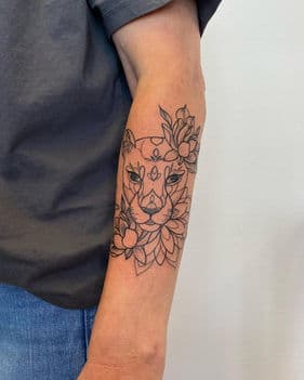 Fineline leeuwin met bloemen en mandala patronen op de onderarm.