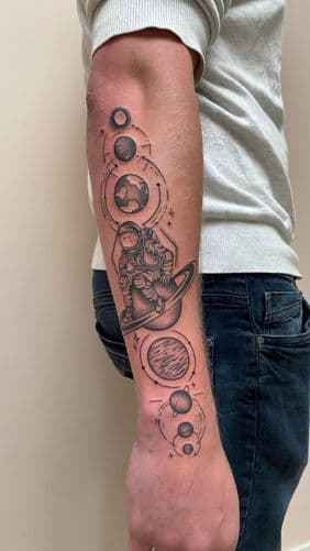 Zwart-wit tattoo van een astronaut zittend op Saturnus, omringd door planeten.