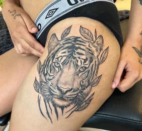 Realistische tijgerkop met bladeren op bovenbeen.