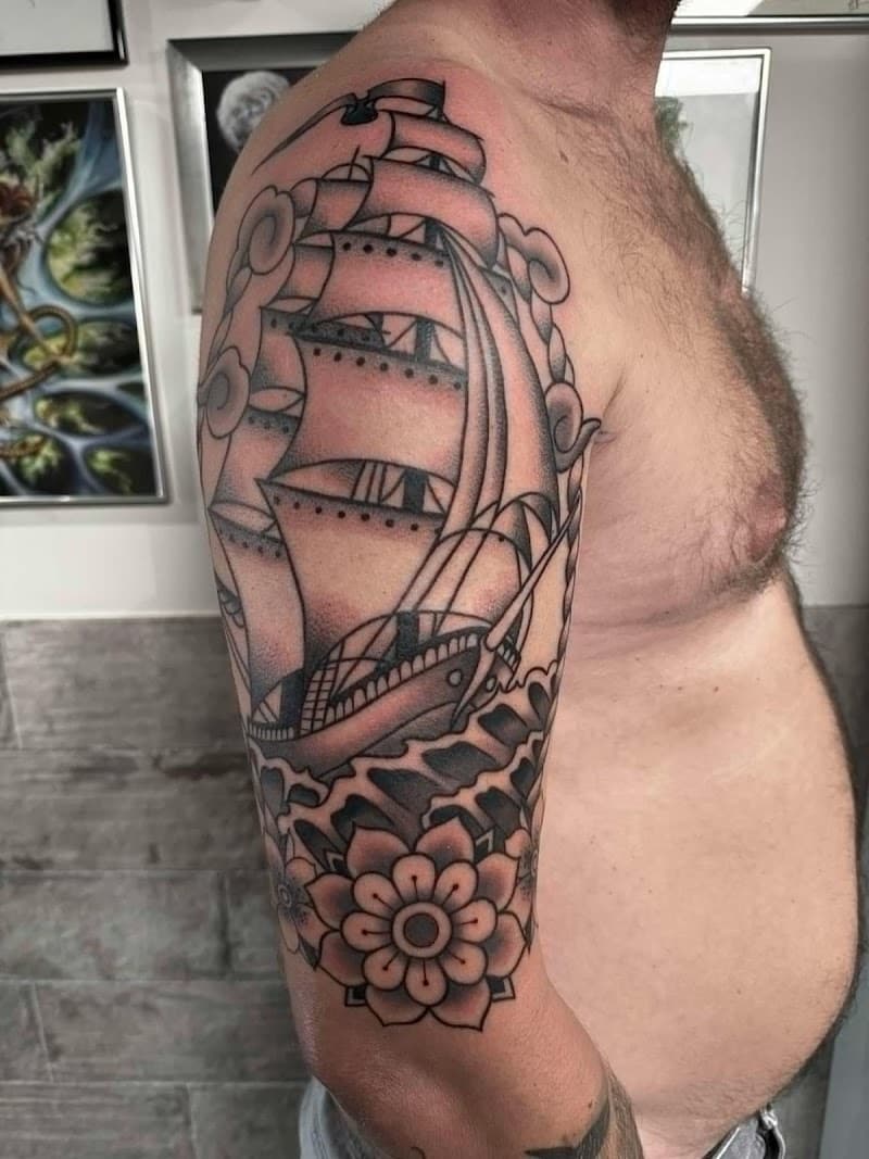 Traditionele tattoo van een zeilschip en bloemen op de bovenarm.