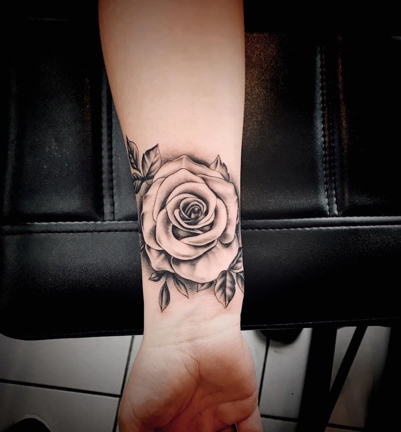 Zwart-grijze roos tattoo op de pols met bladeren.
