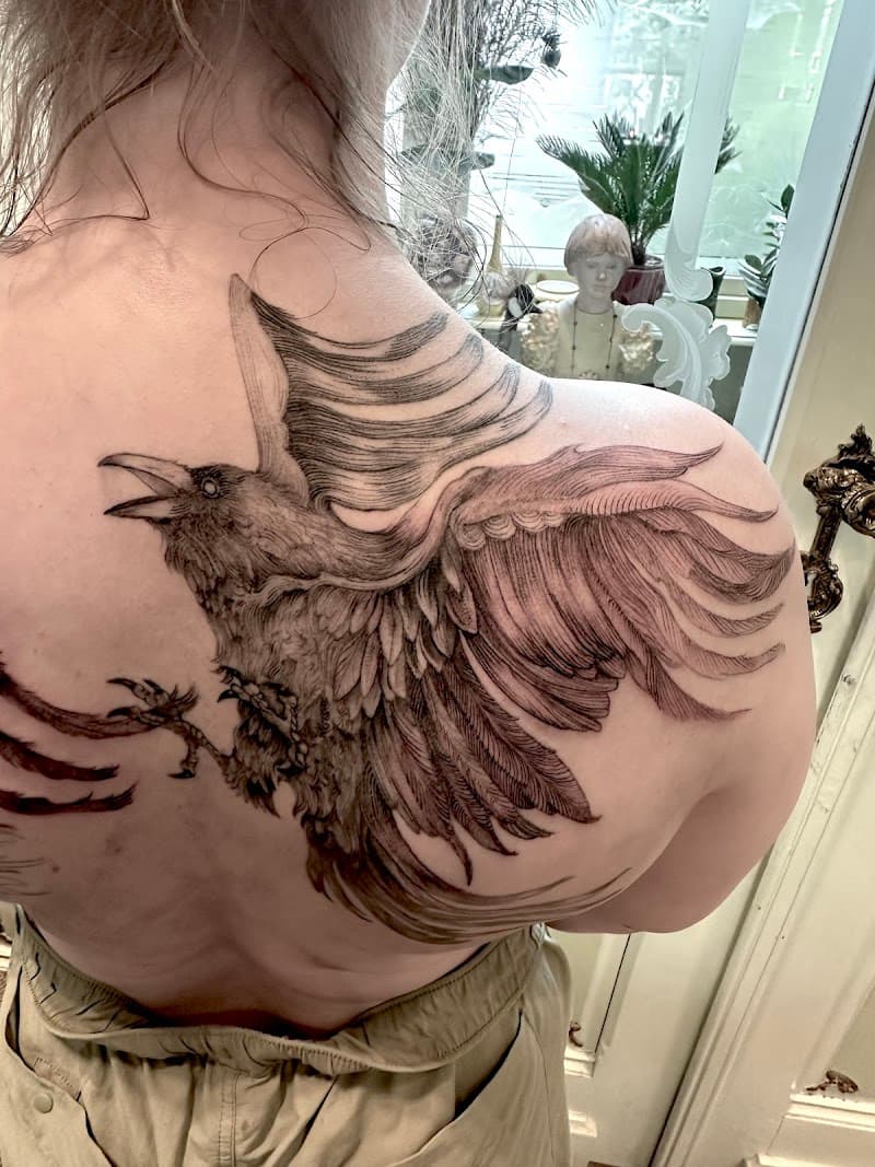 Grote zwart-wit raaf tattoo op het schouderblad.