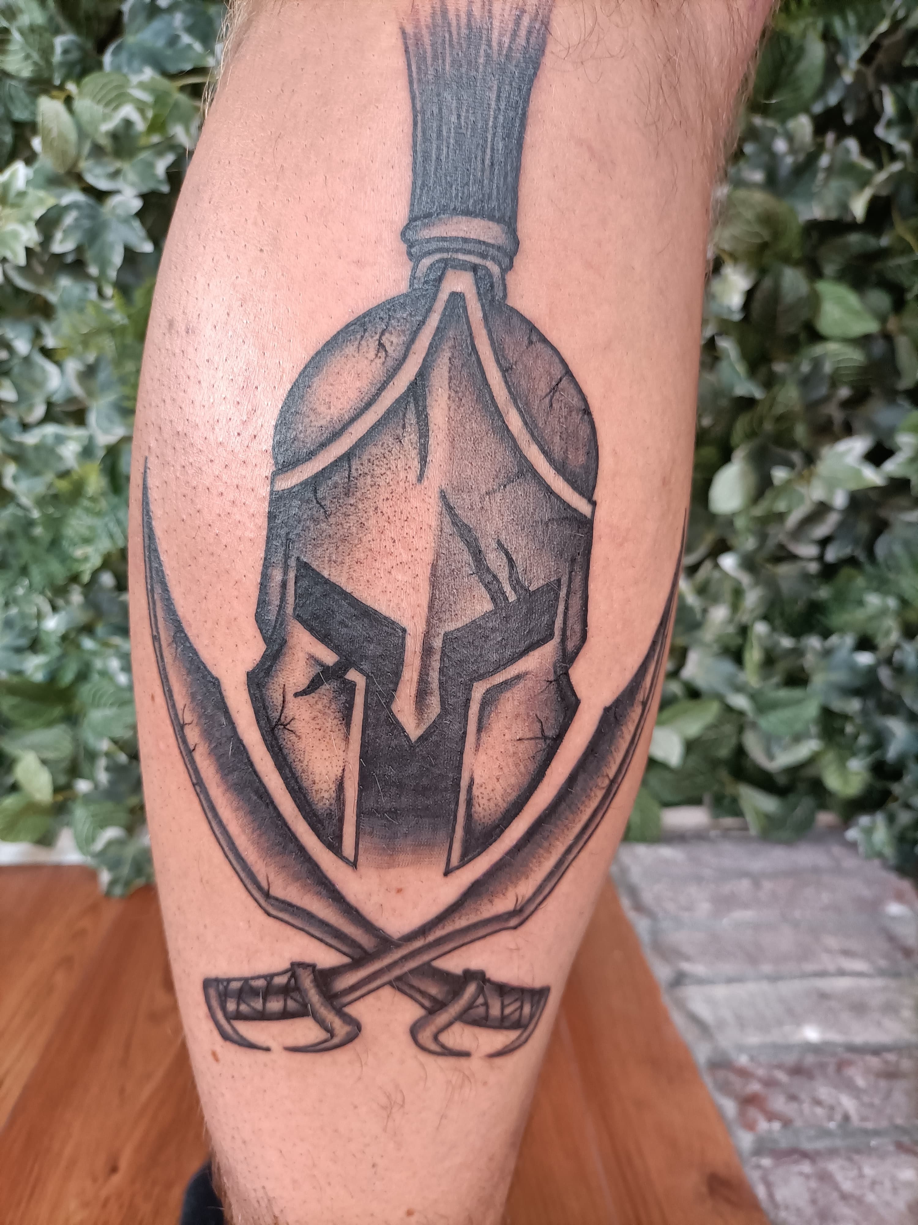 Zwart-wit Spartaanse helm met gekruiste zwaarden op onderbeen.