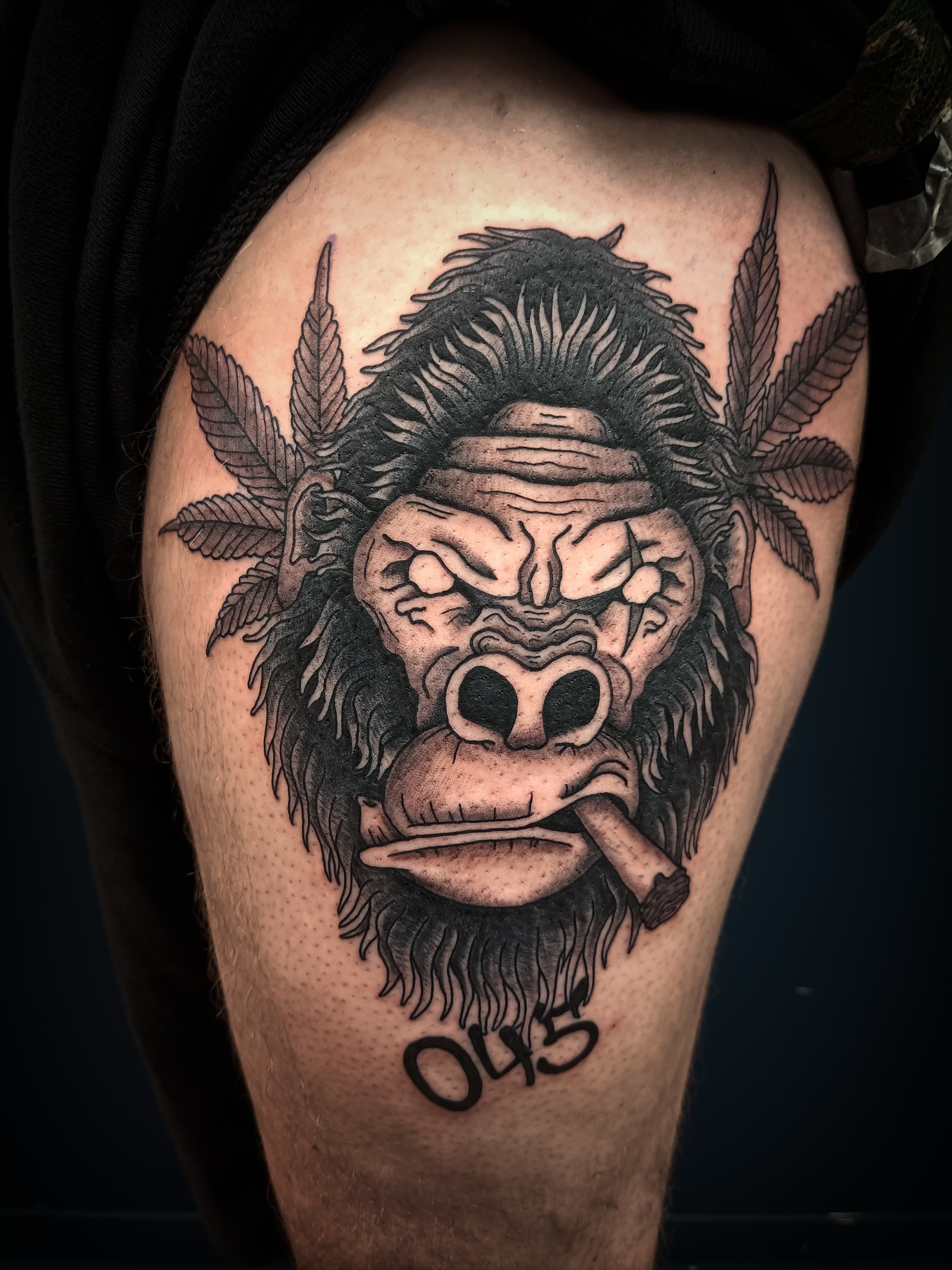 Blackwork tattoo van een gorilla die een sigaar rookt, met wietbladeren en '045'.
