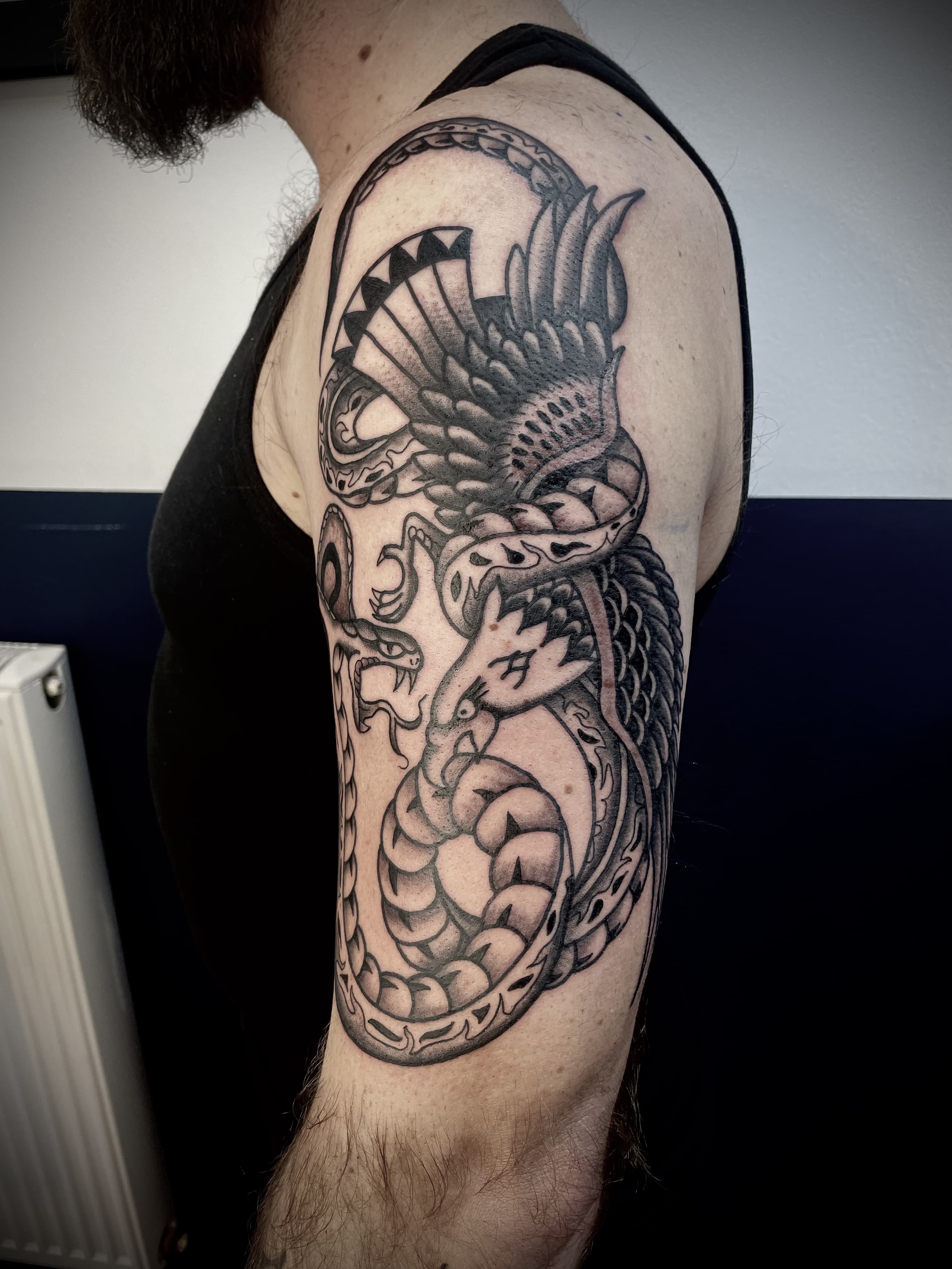 Zwart-wit tattoo van een adelaar die vecht met een slang op de bovenarm.