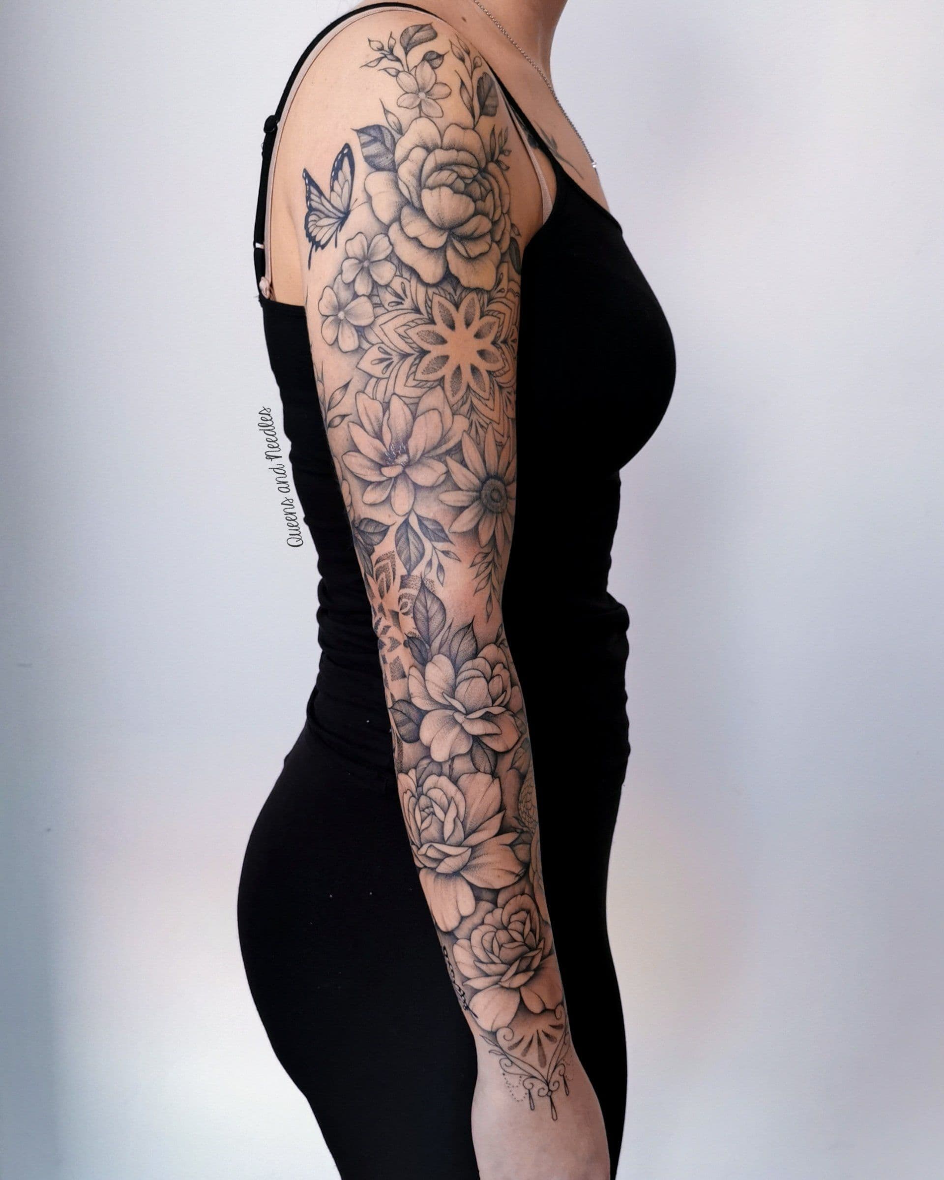 Zwart-wit sleeve tattoo met bloemen, vlinder en mandala.
