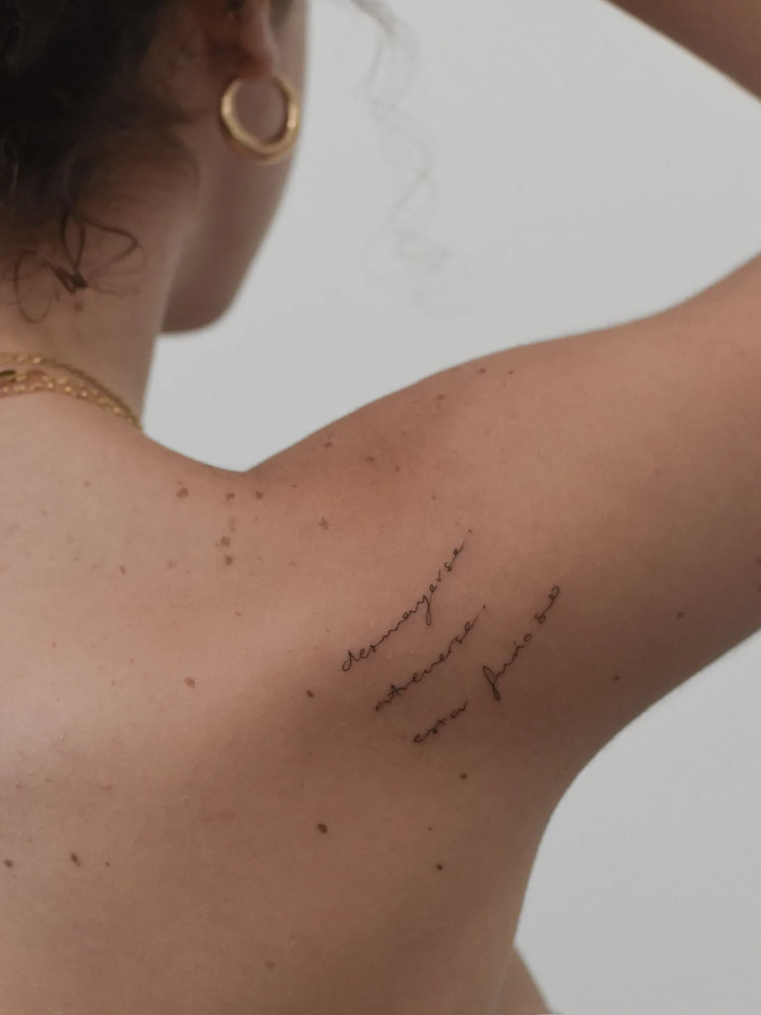 Fineline tekst tattoo op schouderblad, drie regels in sierlijk handschrift.