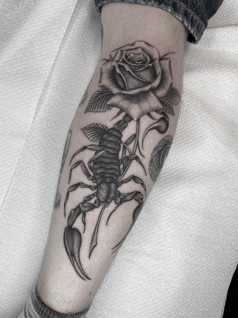 Blackwork schorpioen en roos tattoo op onderbeen.