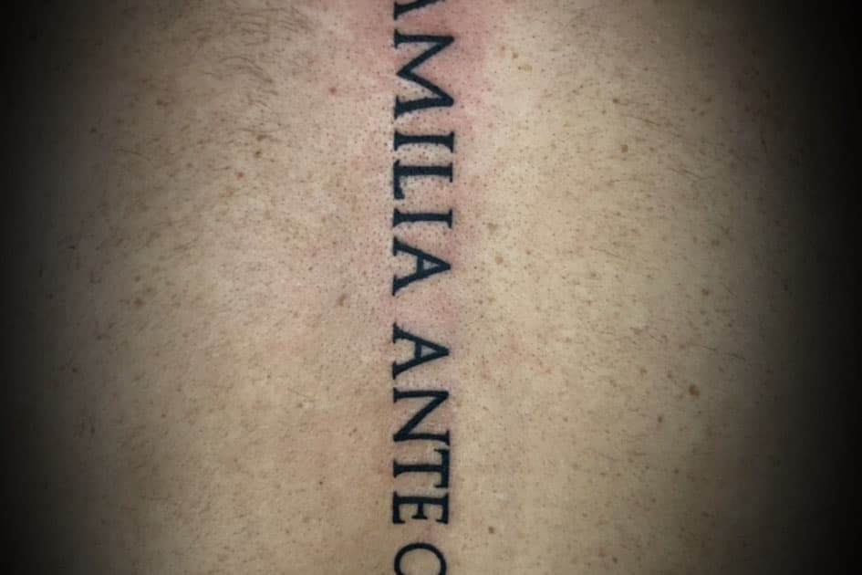 Verticale tekst tattoo 'FAMILIA ANTE OMNIA' op de rug.