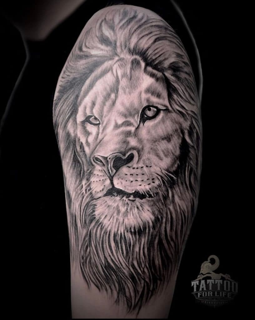 Realistische zwart-wit leeuwenkop tattoo op de bovenarm.