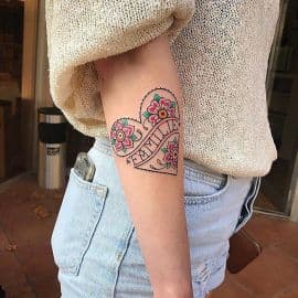 Traditional hart tattoo met bloemen en 'FAMILIE' tekst op bovenarm.