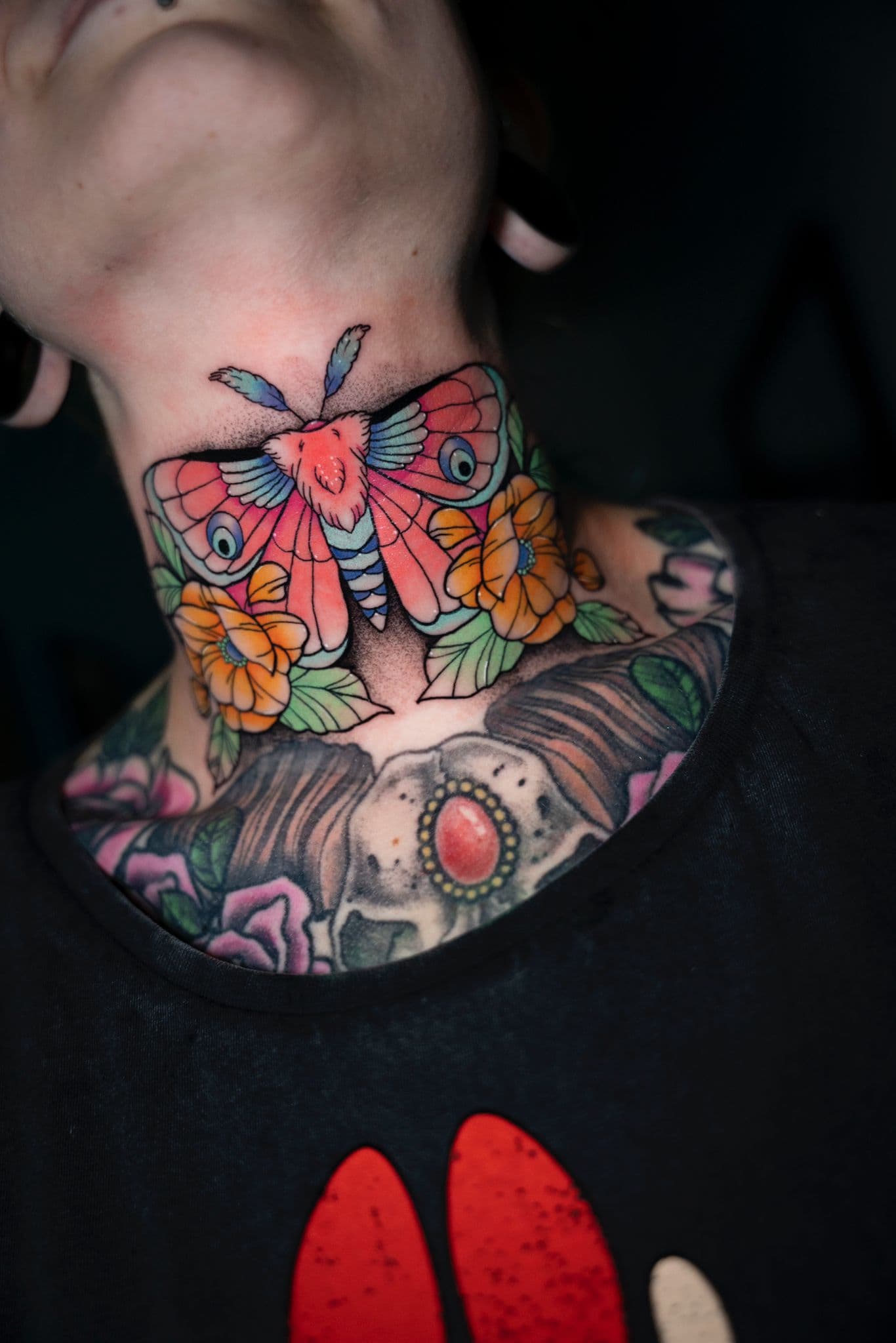 Kleurrijke mot en schedel tattoo op nek en borst.