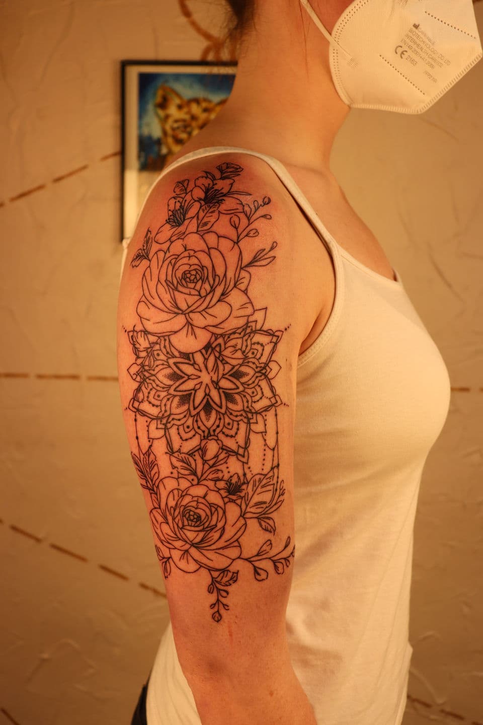 Fineline bloemen en mandala tattoo op bovenarm.