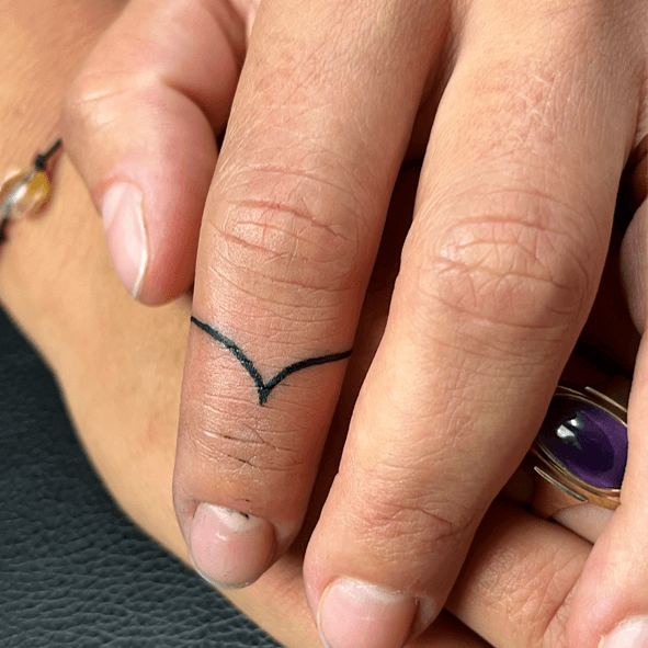 Minimalistische zwarte lijn tattoo in een V-vorm op een vinger.