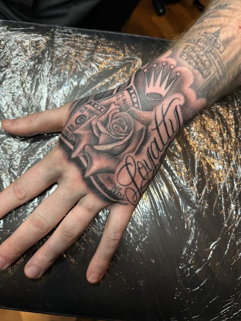 Zwart-wit handtattoo met roos, geld, kroon en 'Loyalty' tekst.