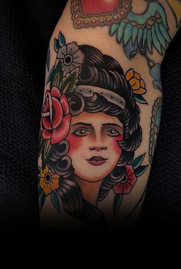 Traditional tattoo van een vrouwenhoofd met bloemen in het haar.