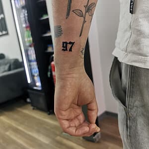 Zwarte '97' nummer tattoo in gotische stijl op de pols.