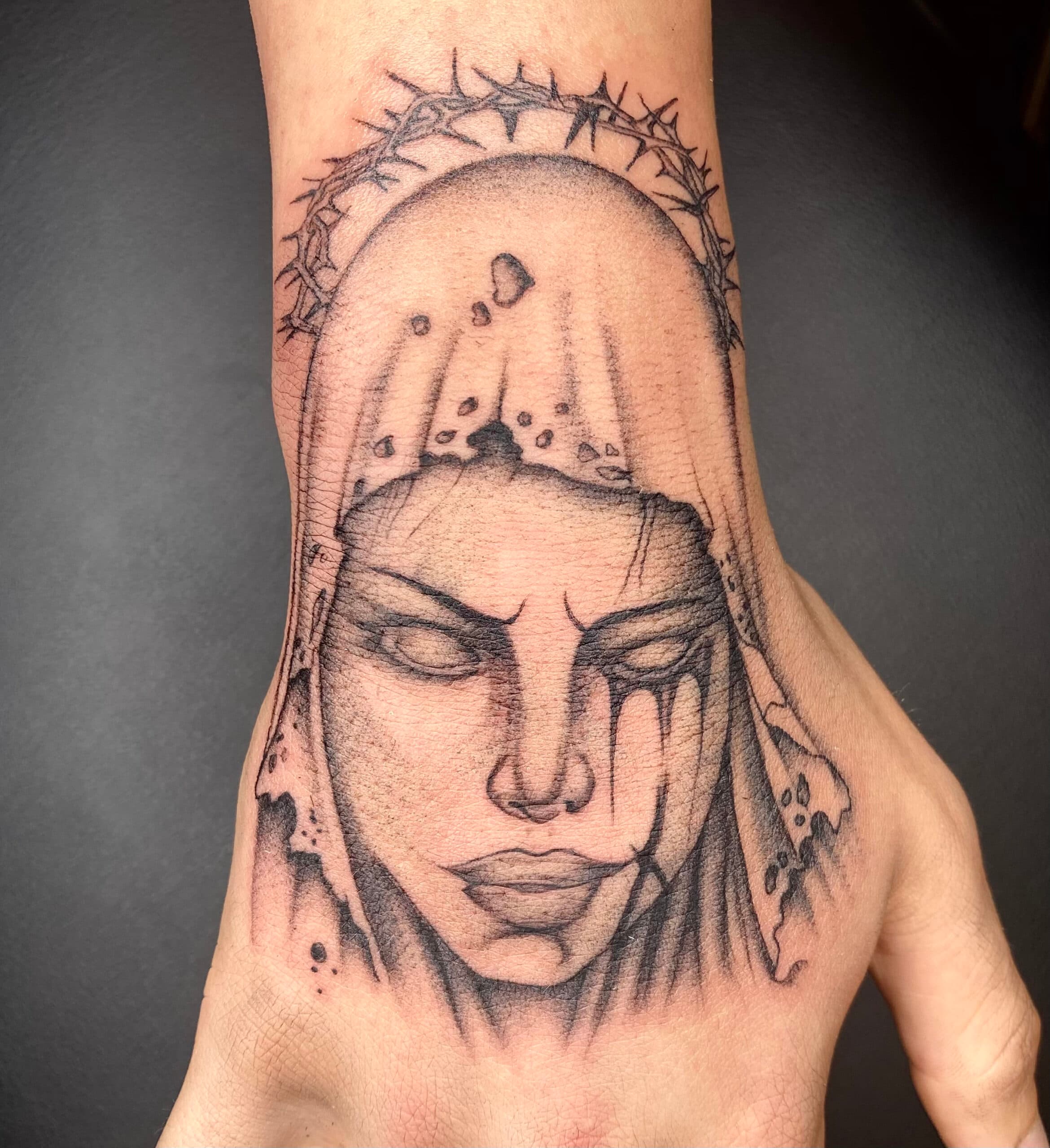 Blackwork tattoo van een huilende vrouw met doornenkroon op de hand.