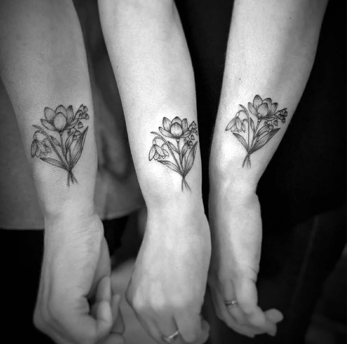Drie identieke fineline bloemenboeket tattoos op polsen.