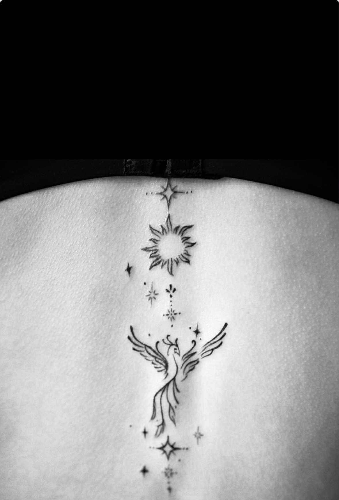 Fineline tattoo van een feniks, zon en sterren op de ruggengraat.