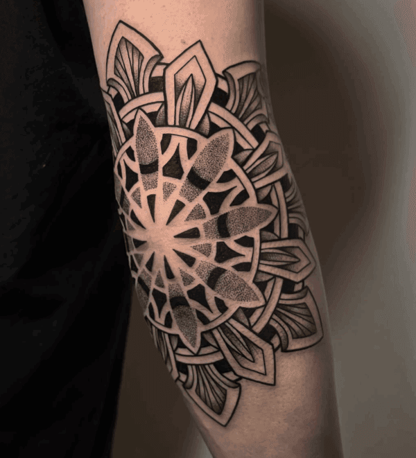 Gedetailleerde mandala tattoo op de elleboog met dotwork en geometrische patronen.