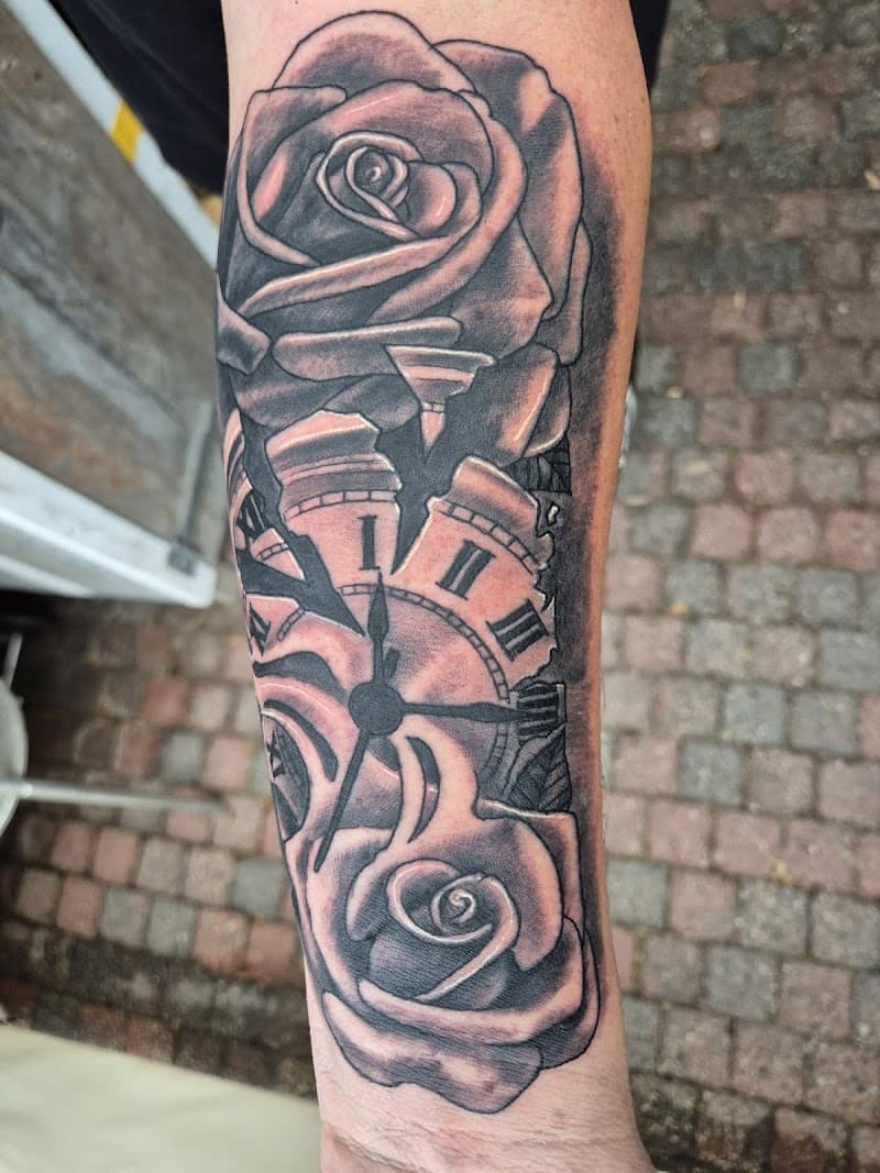 Zwart-wit tattoo van twee rozen en een gebroken klok op de onderarm.