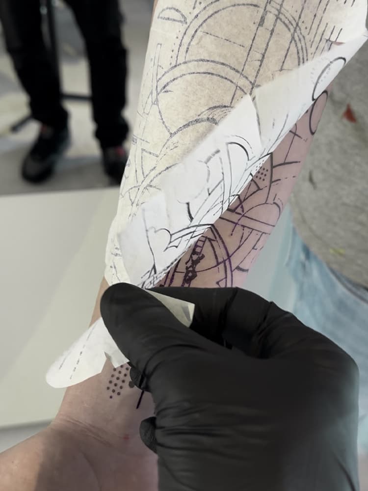 Geometrische tattoo in wording op onderarm, stencil wordt verwijderd.