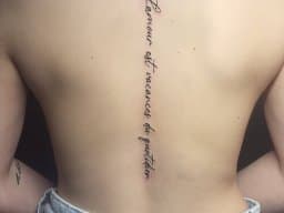 Fineline tekst tattoo op de ruggengraat: "L'amour est vacances du quotidien".